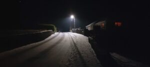 The Derry Road at night. A streetlight illuminates the snow covered road and footpath.